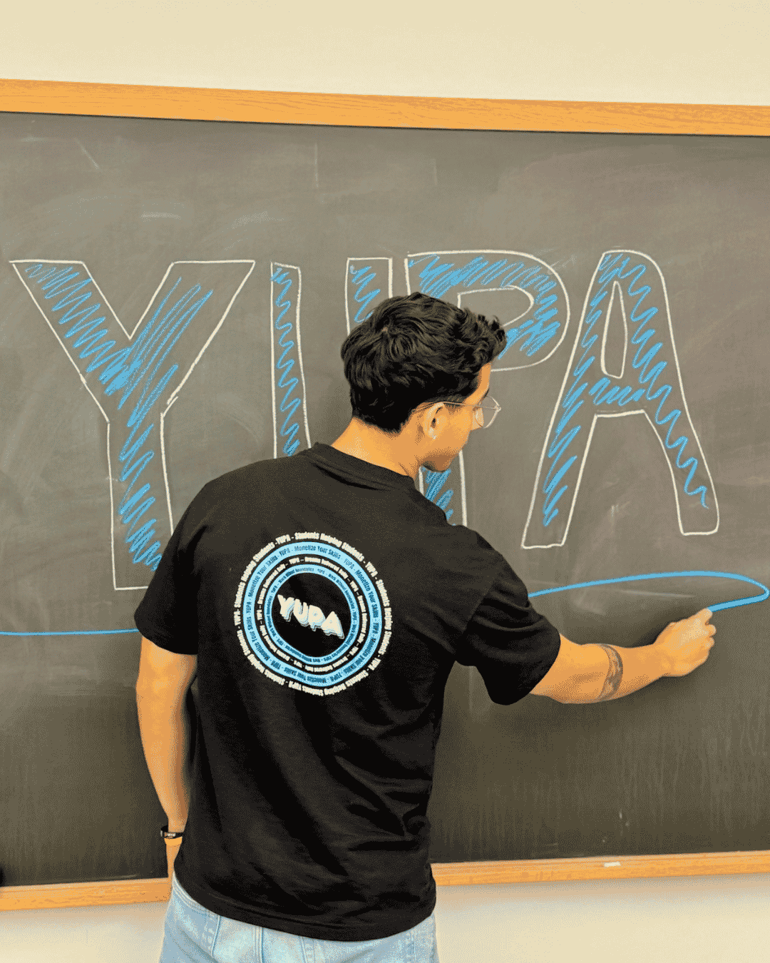 A YUPA student in a branded shirt by a chalkboard